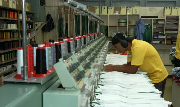 Trabalhador com fone de proteção operando maquinário industrial de costura em uma fábrica.