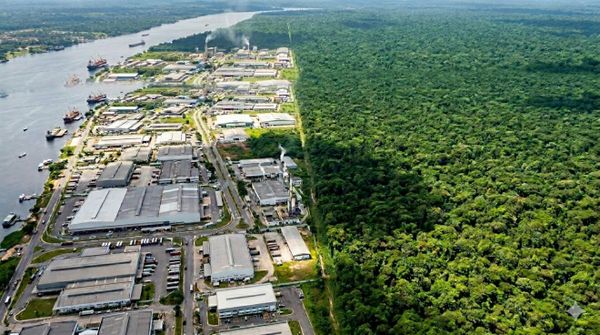Vista aérea do Polo Industrial de Manaus com galpões de fábricas situados ao lado de uma extensa área de floresta preservada.