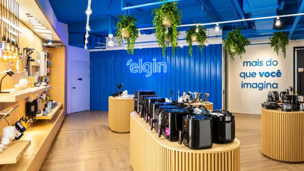 Showroom da Elgin com eletrodomésticos, cafeteiras e fritadeiras elétricas expostos em balcões de madeira e parede azul.