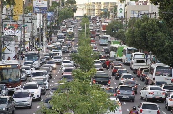 Trânsito intenso de carros e ônibus em avenida movimentada de Manaus, com canteiro central arborizado e prédios ao fundo.