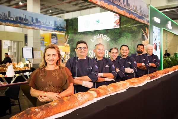 Padeiros uniformizados posam atrás de um pão gigante em formato de baguete durante a Feira de Panificação da Amazônia.