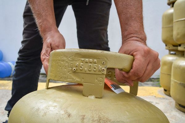 Mãos de um homem segurando a alça de uma botija de gás de cozinha de cor bege em Manaus.