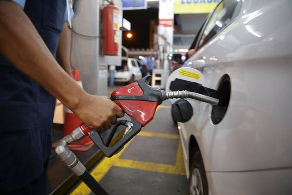 Frentista segura bico de bomba de combustível vermelha enquanto abastece carro branco em posto de Manaus.