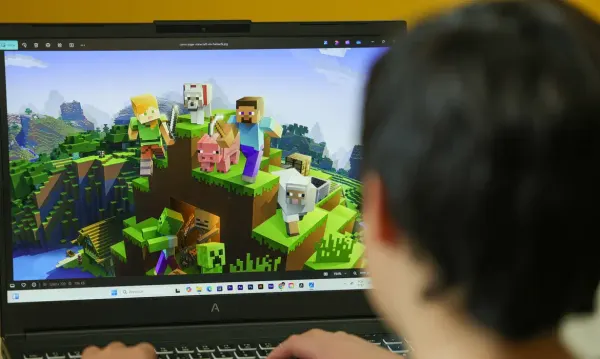 Pessoa de costas jogando Minecraft em um notebook preto da marca Avell.