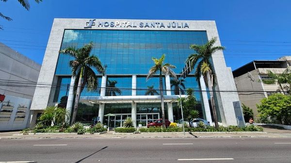 Fachada do Hospital Santa Júlia em Manaus, com vidros espelhados azuis e palmeiras na frente sob céu limpo.