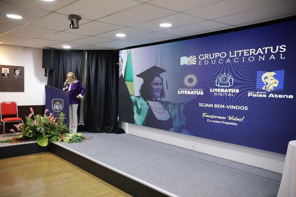 Mulher discursa em púlpito ao lado de telão com a marca Grupo Literatus Educacional durante evento em Manaus.