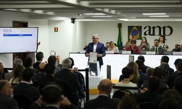 Homem de terno azul segura documento diante de plateia e telão durante leilão na sede da ANP, no Rio de Janeiro.