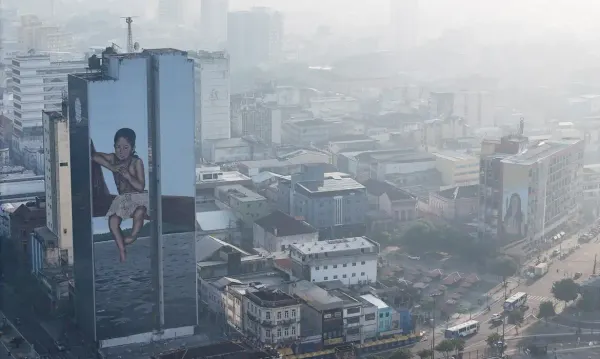 Vista aérea do Centro de Manaus coberto por fumaça, com destaque para um prédio com grafite de uma criança indígena.