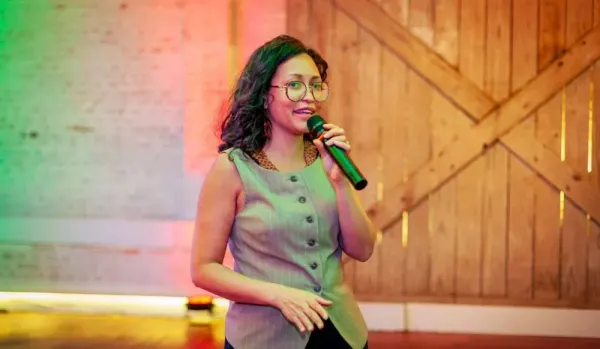 Mona Oliveira, fundadora e CEO da BioLinker, fala ao microfone durante evento em ambiente com iluminação cênica.