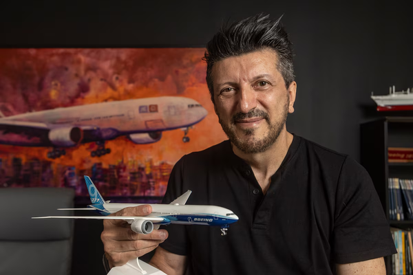 Lito Sousa sorri segurando uma miniatura de avião da Boeing, com um quadro de aeronave ao fundo.