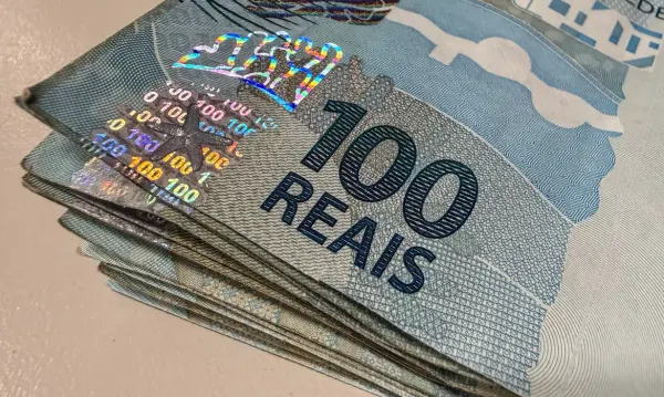 Maço de notas de cem reais empilhadas sobre uma superfície clara.