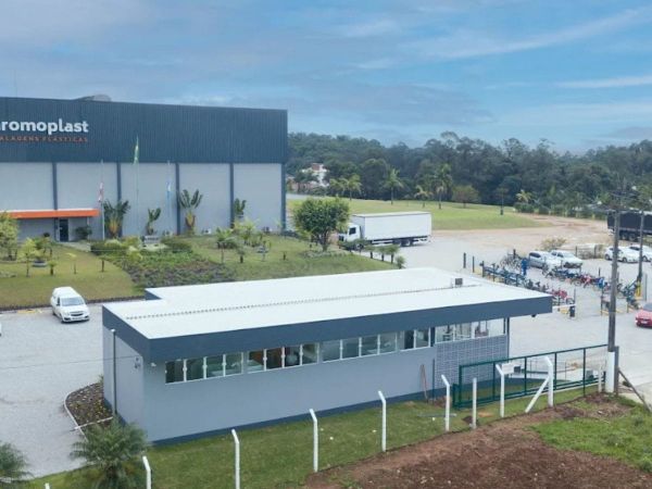 Fachada da unidade da Chromoplast Embalagens Plásticas com pátio de estacionamento e área verde ao fundo.