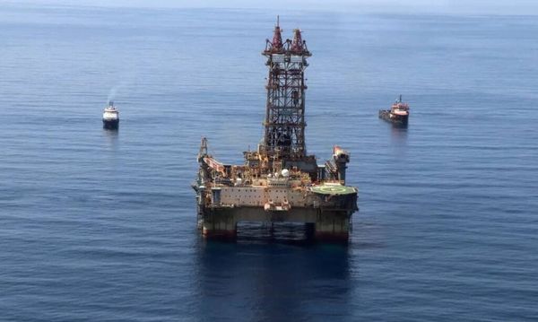 Plataforma de petróleo em operação no mar, acompanhada por dois navios de apoio em águas azuis.