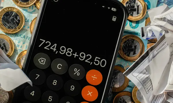 Celular exibindo aplicativo de calculadora sobre moedas de Real e notas de dinheiro.