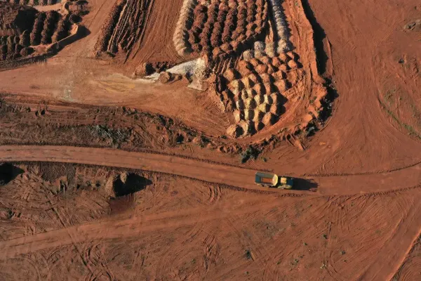 Vista aérea de uma área de mineração com terra avermelhada e um caminhão trafegando por uma estrada de terra.
