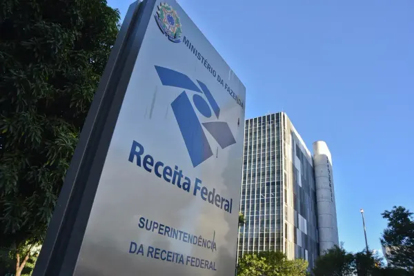 Placa azul e branca com o logotipo da Receita Federal e os dizeres Superintendência da Receita Federal em frente a um prédio.