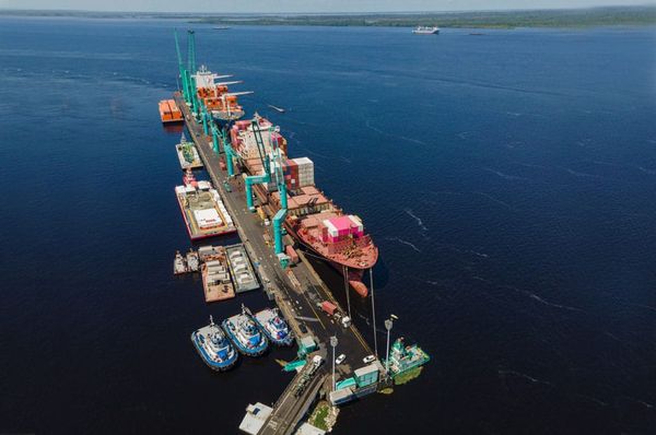 Vista aérea do Super Terminais em Manaus com navio de carga atracado, contêineres coloridos e guindastes operando no rio.
