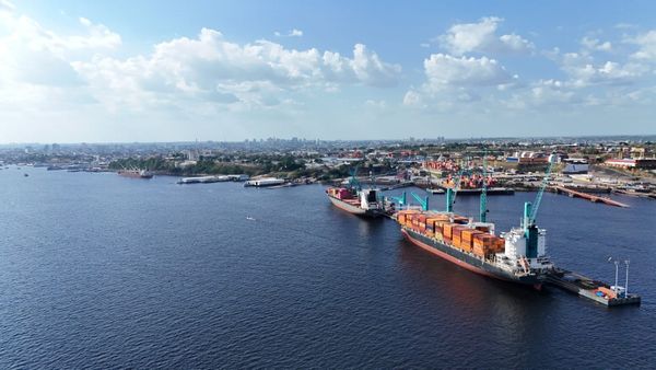 Navios cargueiros atracados no Super Terminais em Manaus, com guindastes operando contêineres sob céu aberto.