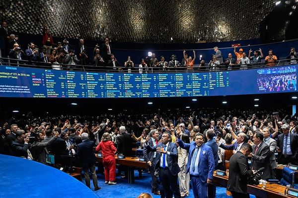 Plenário do Senado Federal com painel eletrônico exibindo resultado de votação e senadores comemorando no centro.