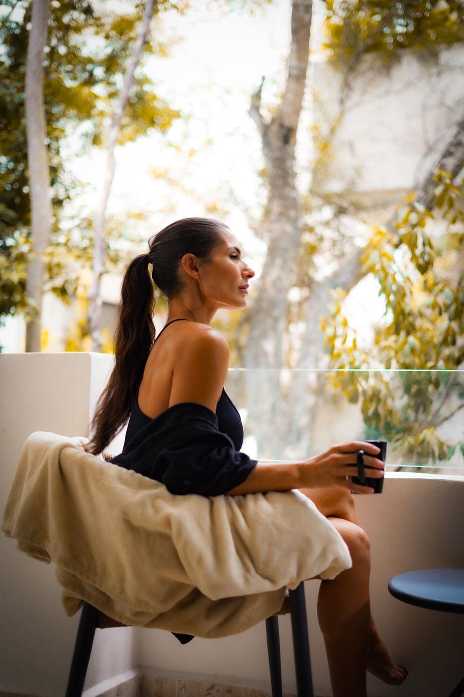 A woman sitting quietly with a warm drink, looking out at the trees