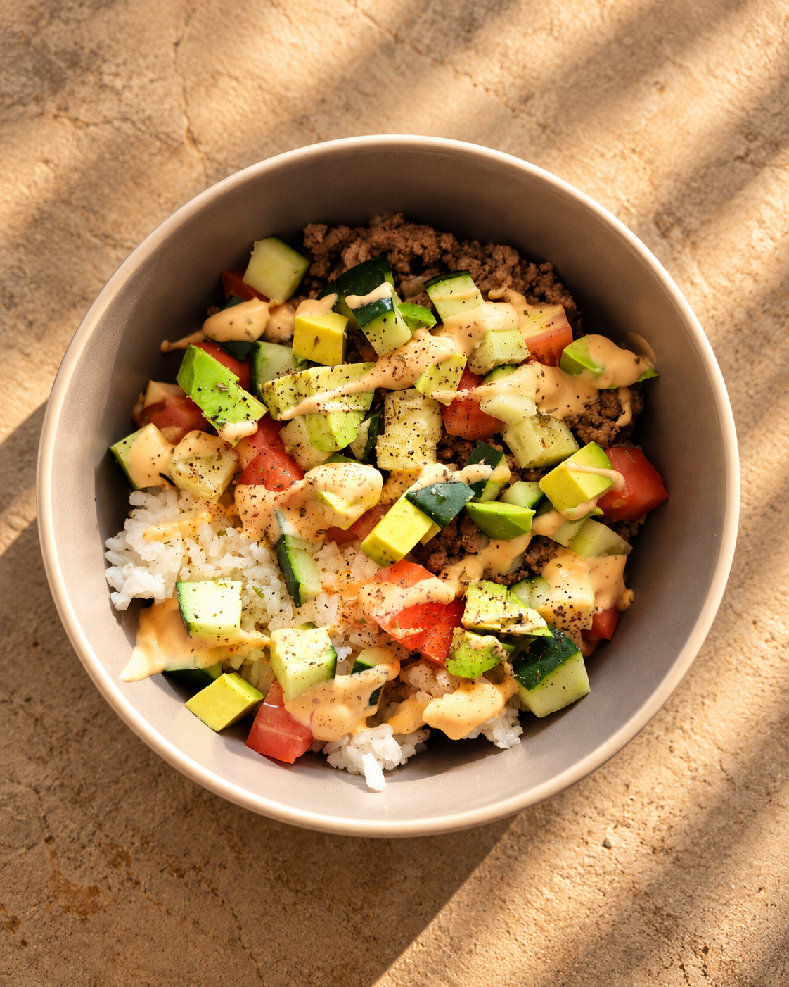Rice bowl with ground meat, avocado, cucumber, tomato and creamy sauce