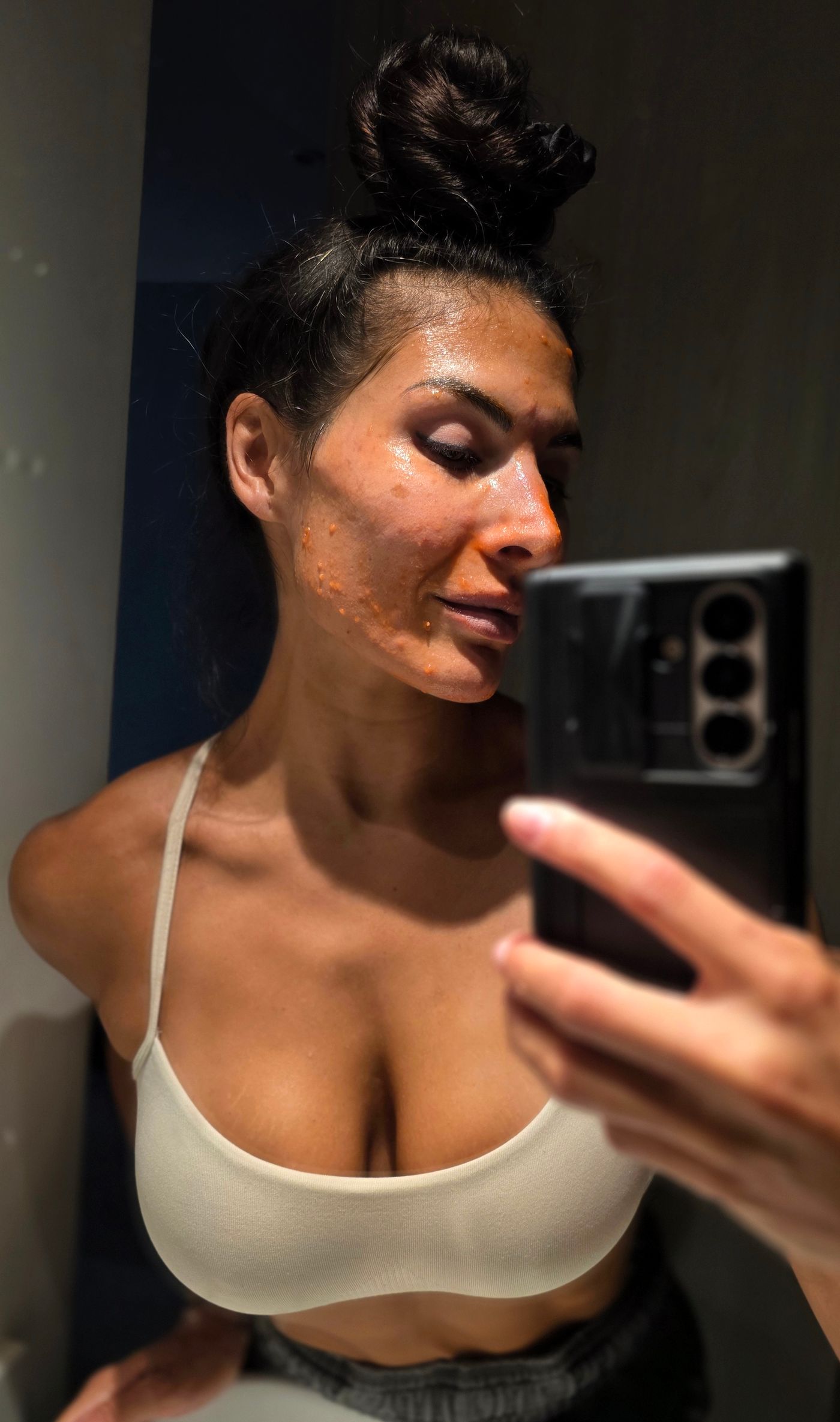 Savannah taking a mirror selfie with a papaya mask on her face.
