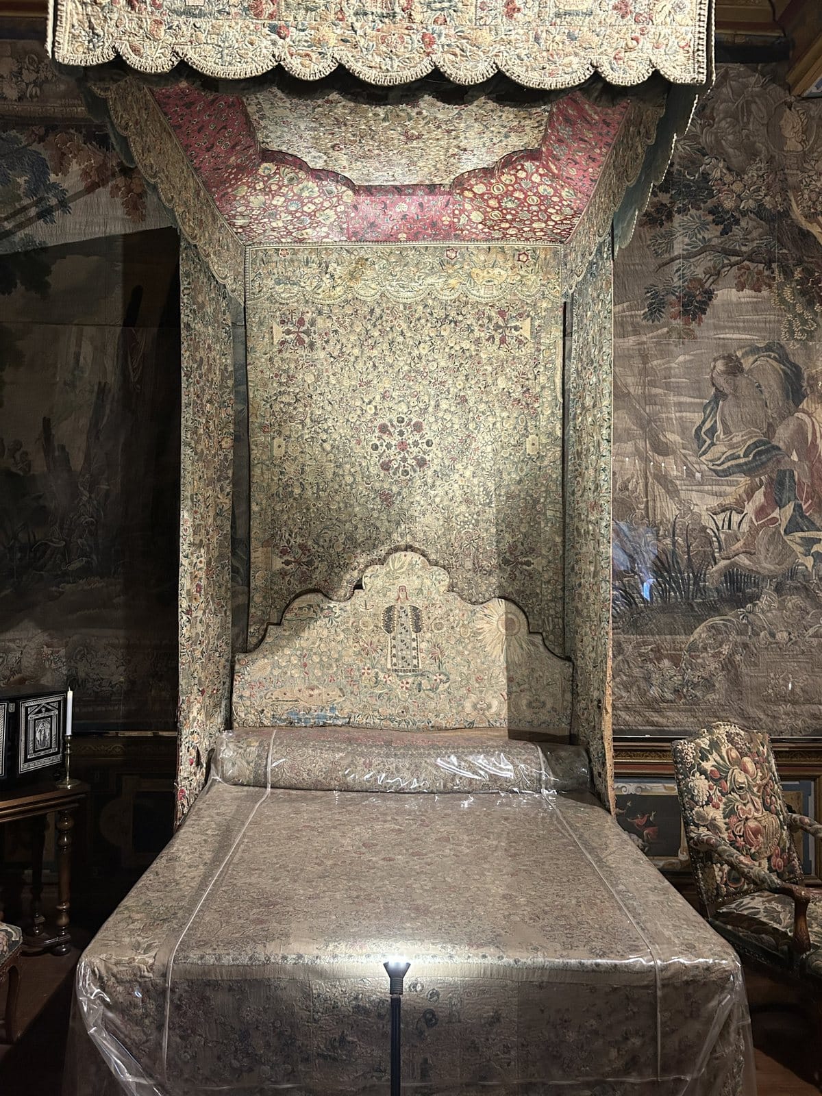An embroidered four-poster bed protected by a clear plastic cover