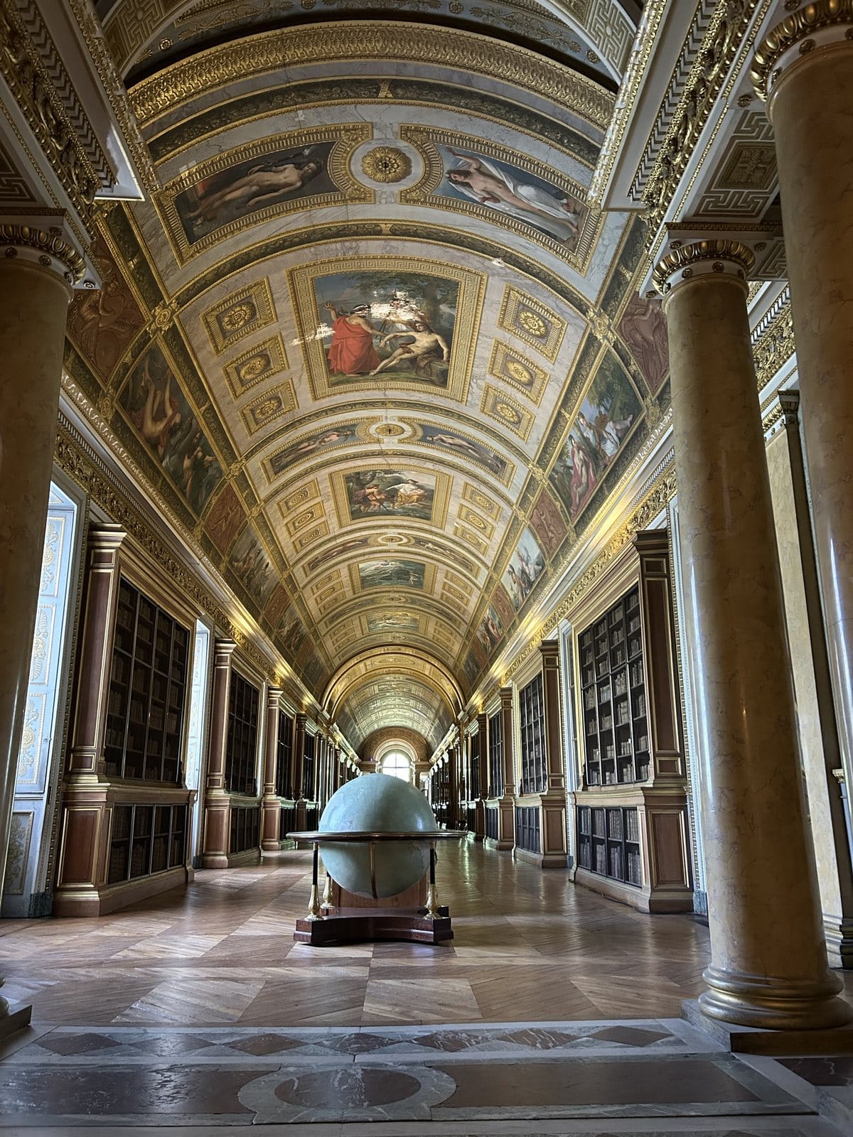 A long gallery at Fontainebleau with a painted ceiling, bookcases and a large globe