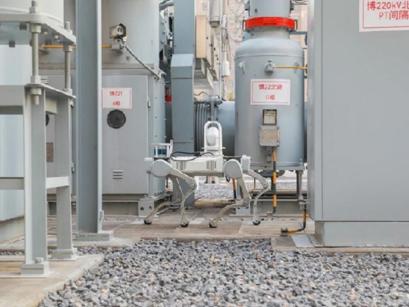 A DEEP Robotics quadruped robot walking between tanks and switchgear at an electrical power site.