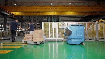 Siasun's blue 星卫来 industrial cleaning robot on a green factory floor beside two workers moving boxes on a pallet
