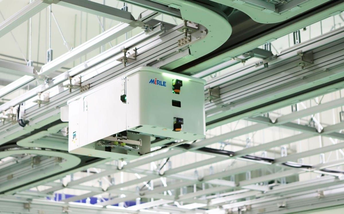 A white Mirle overhead hoist transfer vehicle hanging from ceiling tracks inside a factory