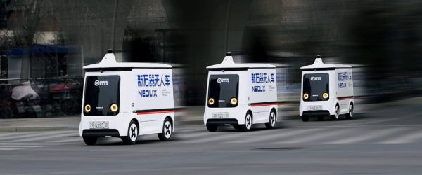 Three white Neolix driverless delivery vans with SF Express branding drive in a line along a city road.