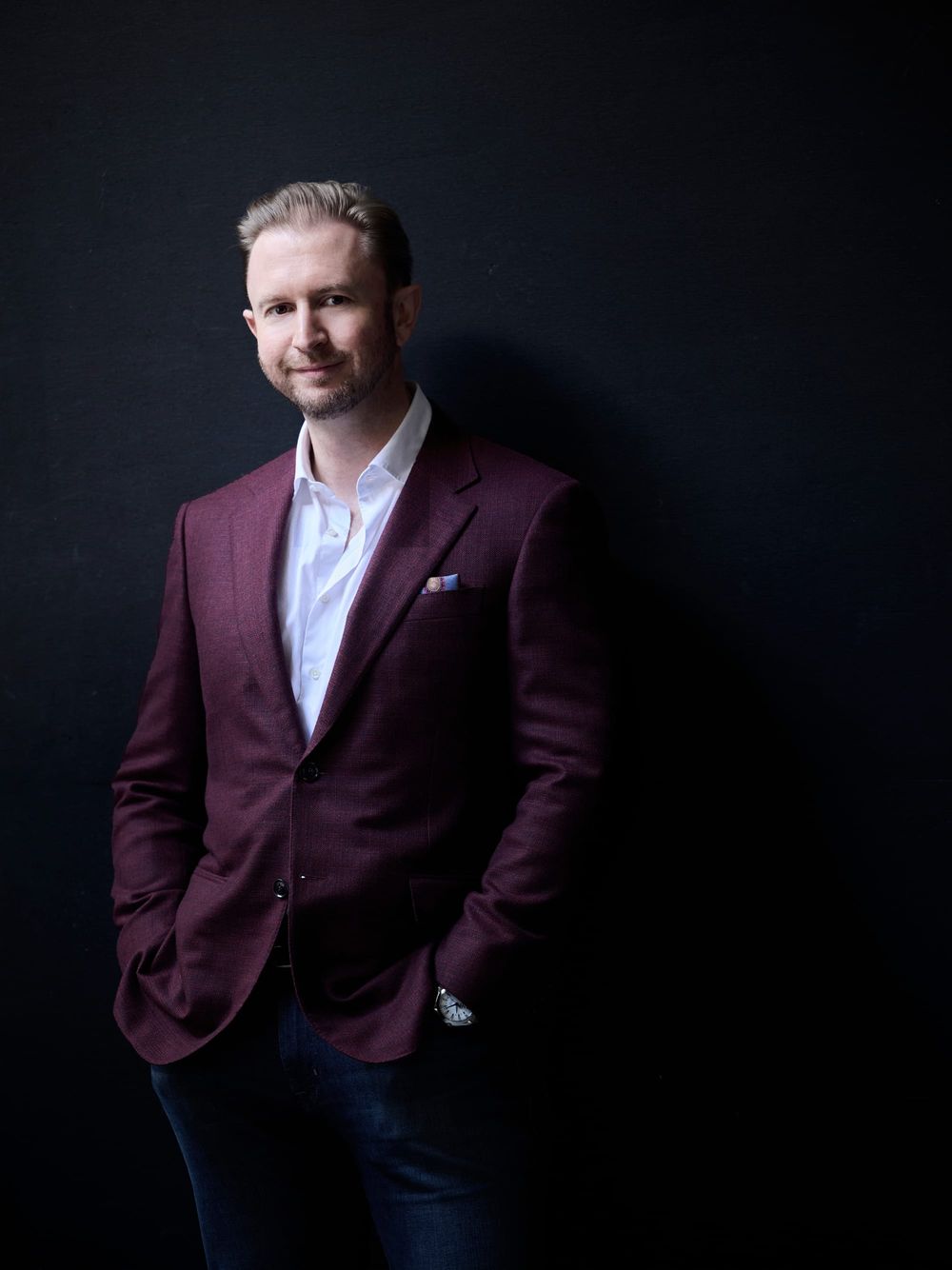 Robert Winter standing against a dark background, wearing a claret jacket and white open-necked shirt.