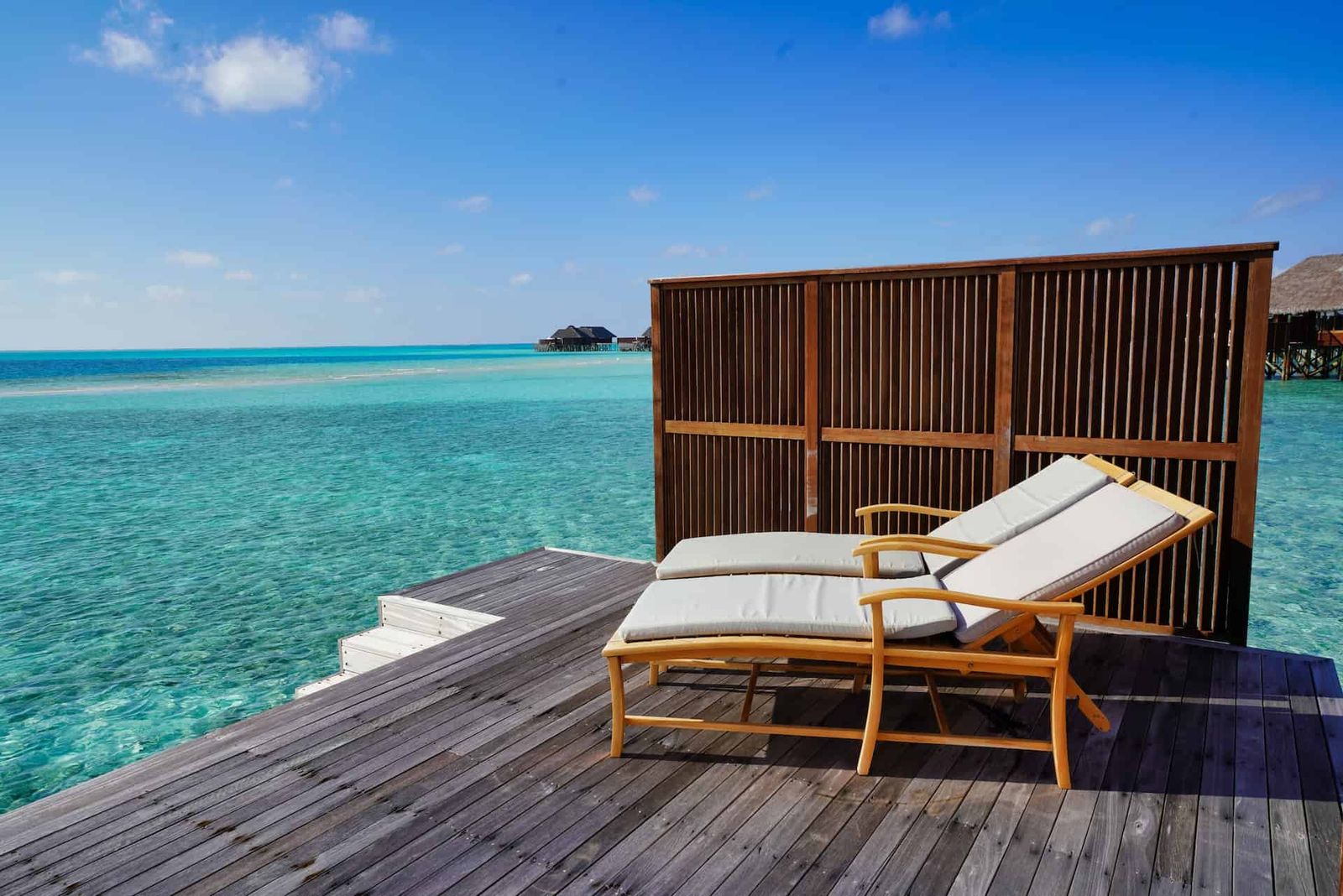 Two deck chairs beside a crystal clear light blue sea.