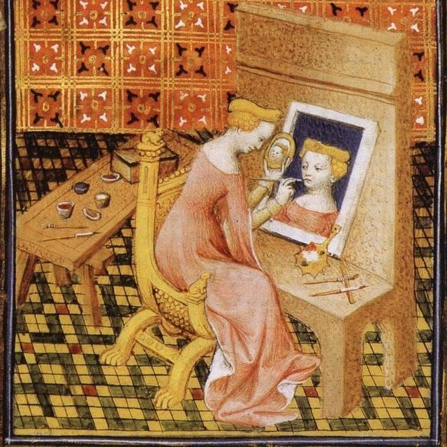 Medieval illustration of a woman painting her own portrait while holding a mirror, seated at a table with brushes and pigments, symbolising reflection and self-observation.