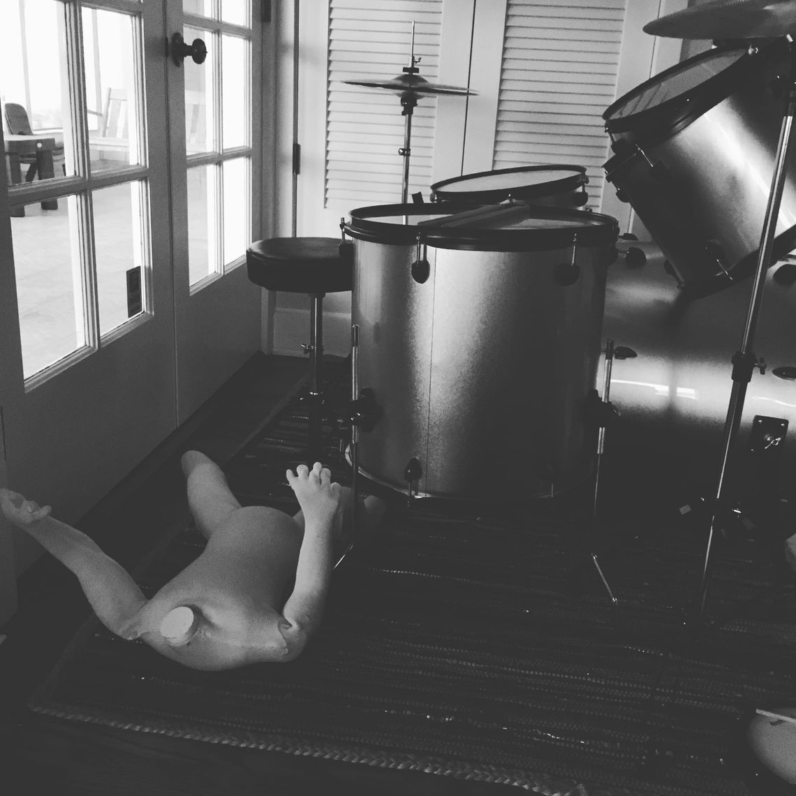A headless, childsize mannequin with poseable joints and a fabric skin lies on its back next to a cheap drumset in my house.
