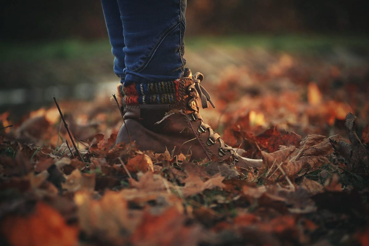 Boots and jeans standing amid rich brown and orange fallen autumn leaves