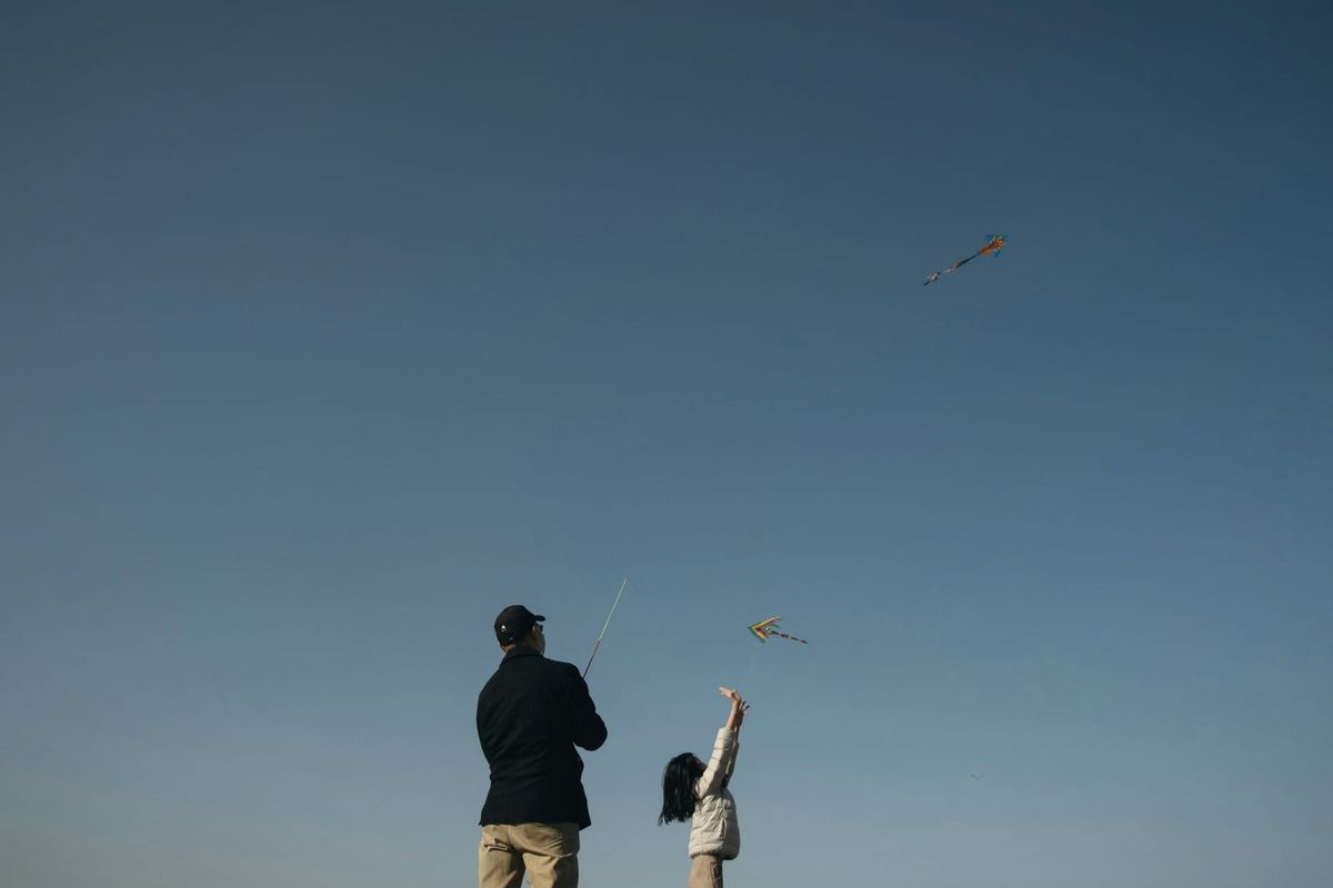 A man and a small girl flying a kite against a clear blue sky
