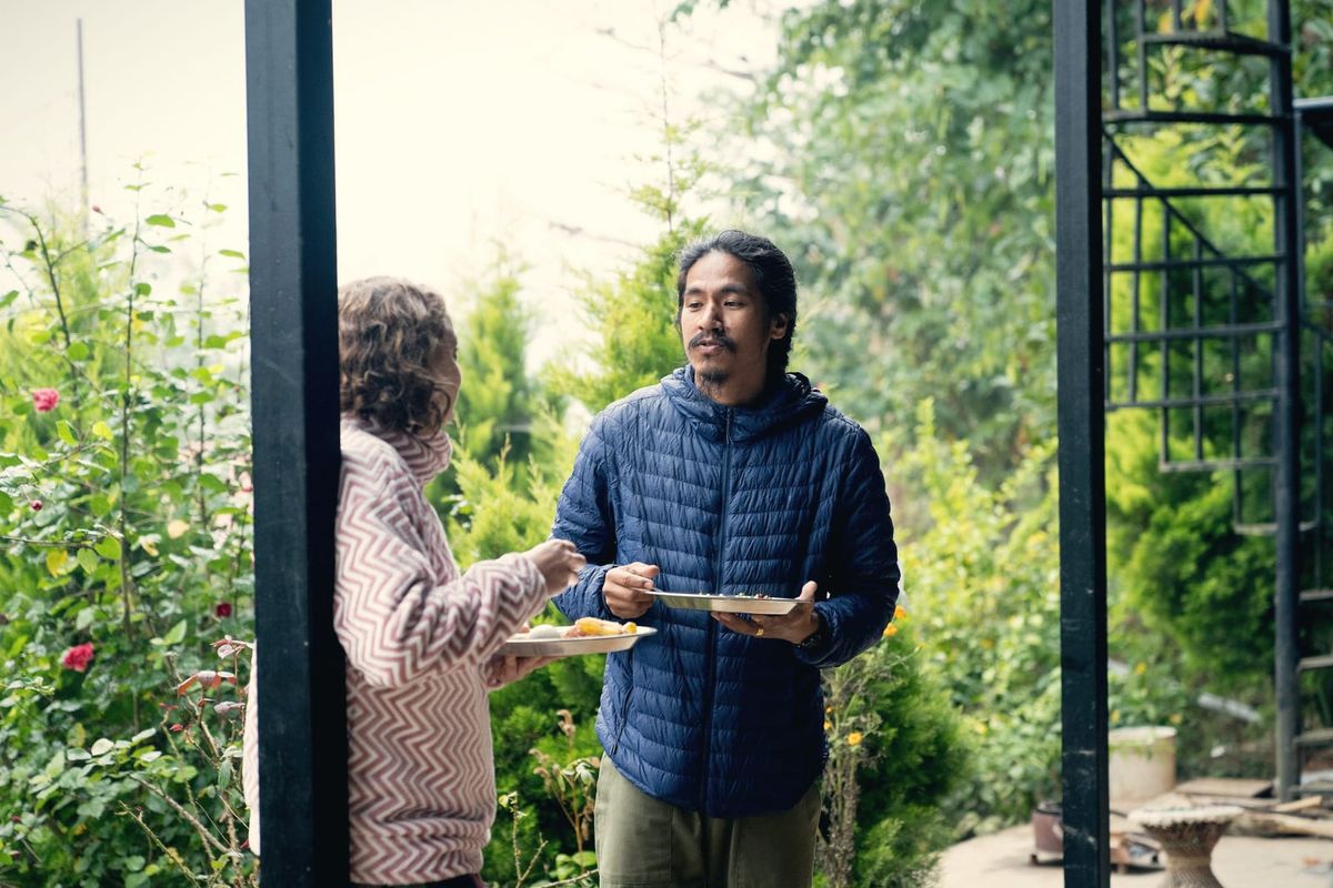 Two people sharing plates of food in a green garden doorway