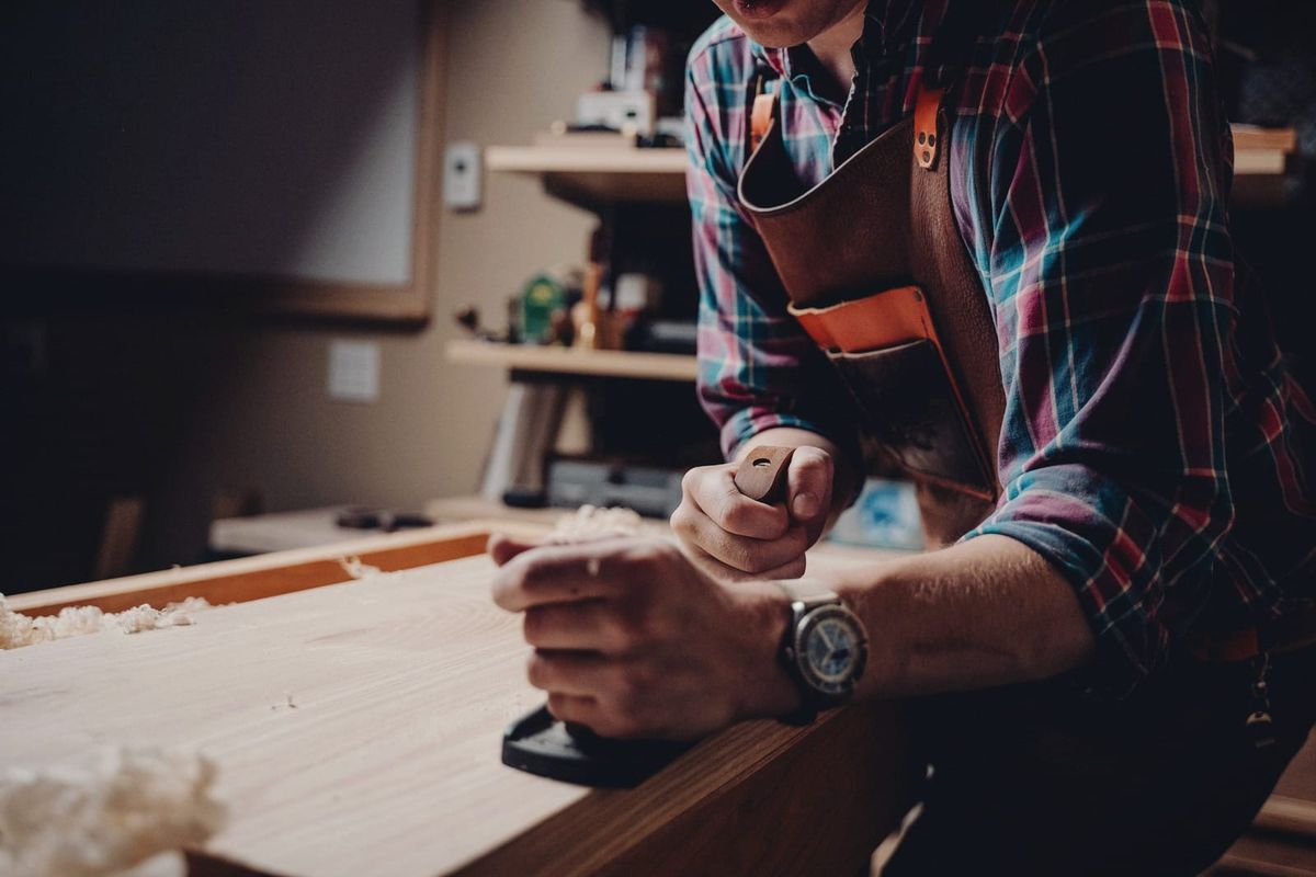 Close-up of a woodworker's hands guiding a plane along a board in warm workshop light