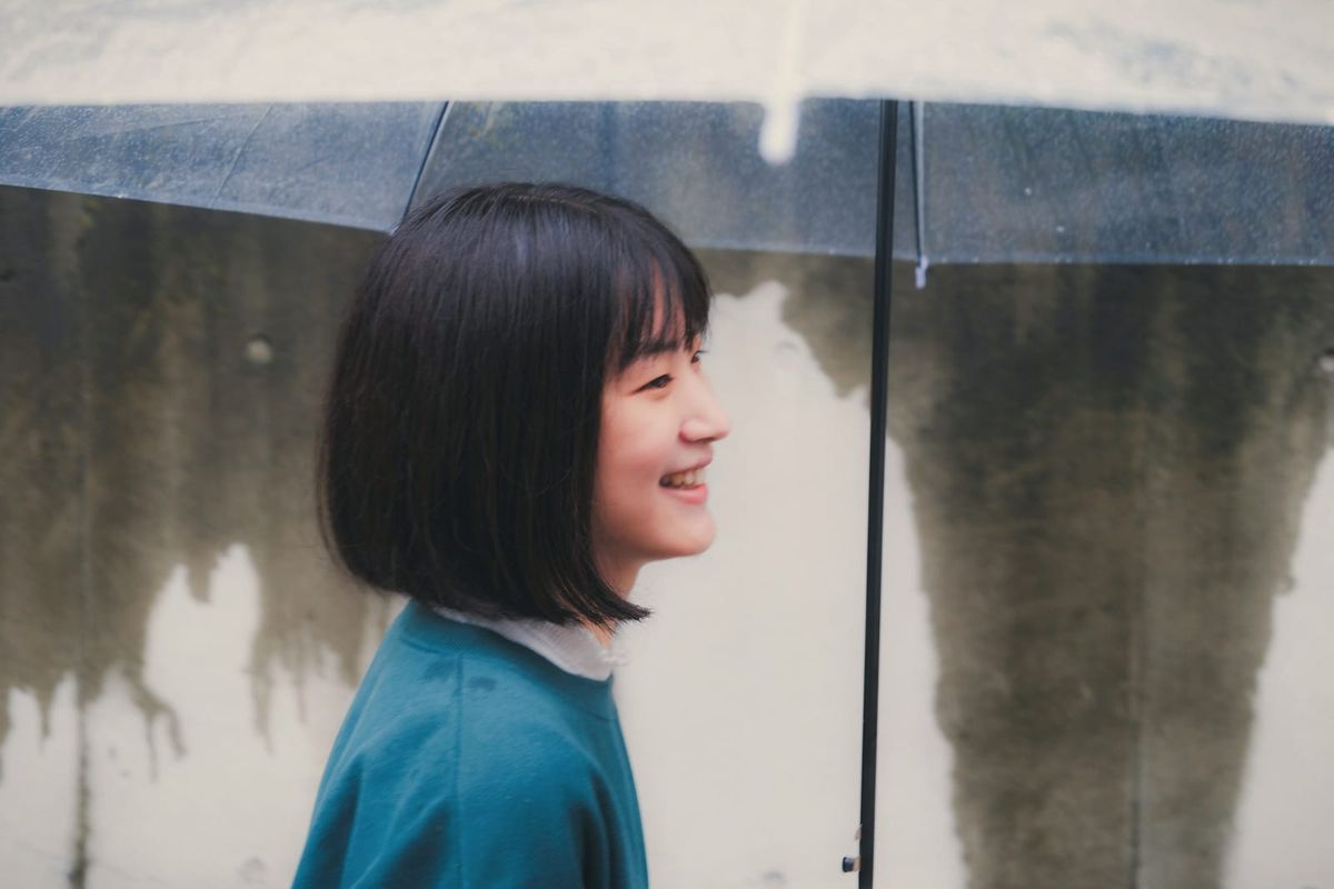 A young woman smiling under a clear umbrella on a rainy day