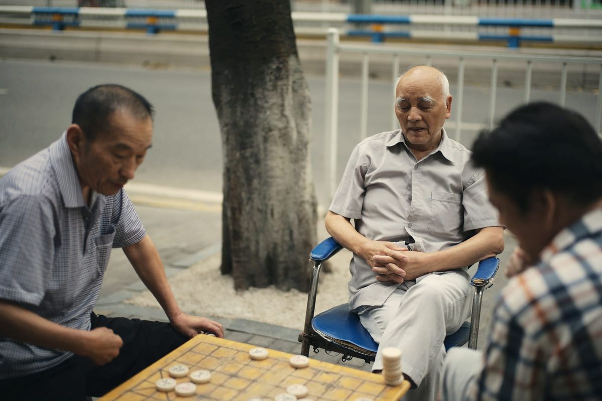 Three older men gathered around a game of xiangqi on a city pavement