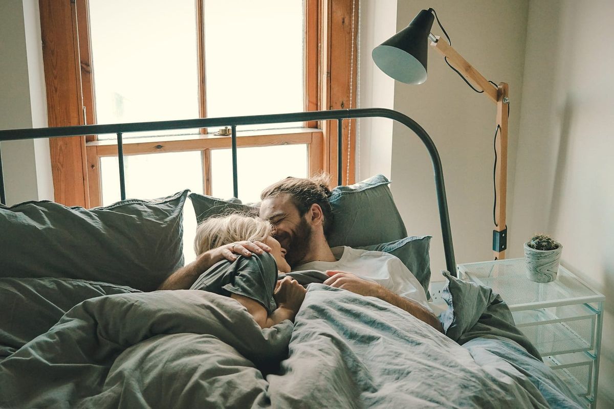 A couple waking up slowly together in bed beside a sunny window