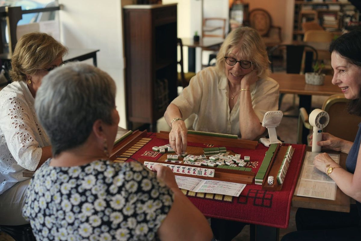 Four older women absorbed in a game of mahjong at a cafe table