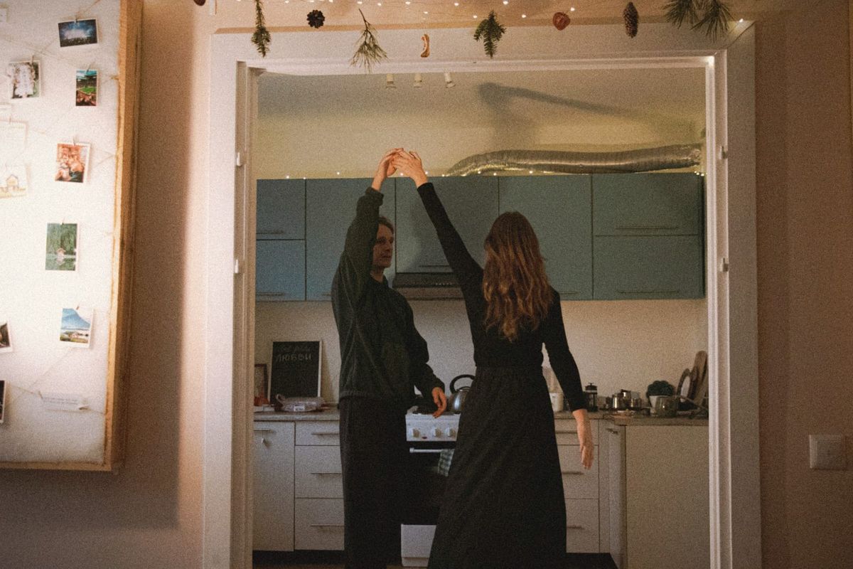 A couple dancing in their kitchen doorway beneath fairy lights