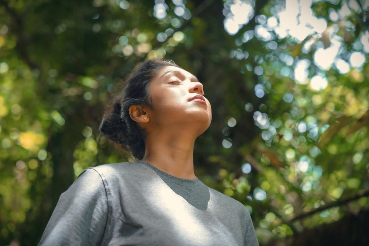 A woman with her face lifted to dappled sunlight, eyes closed, breathing in