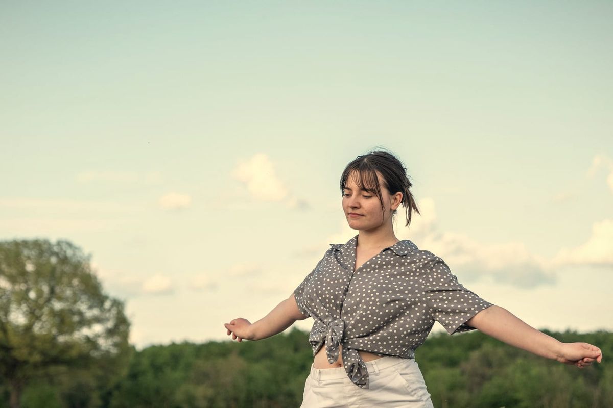 A woman dancing loosely with her arms out under a wide sky, eyes closed
