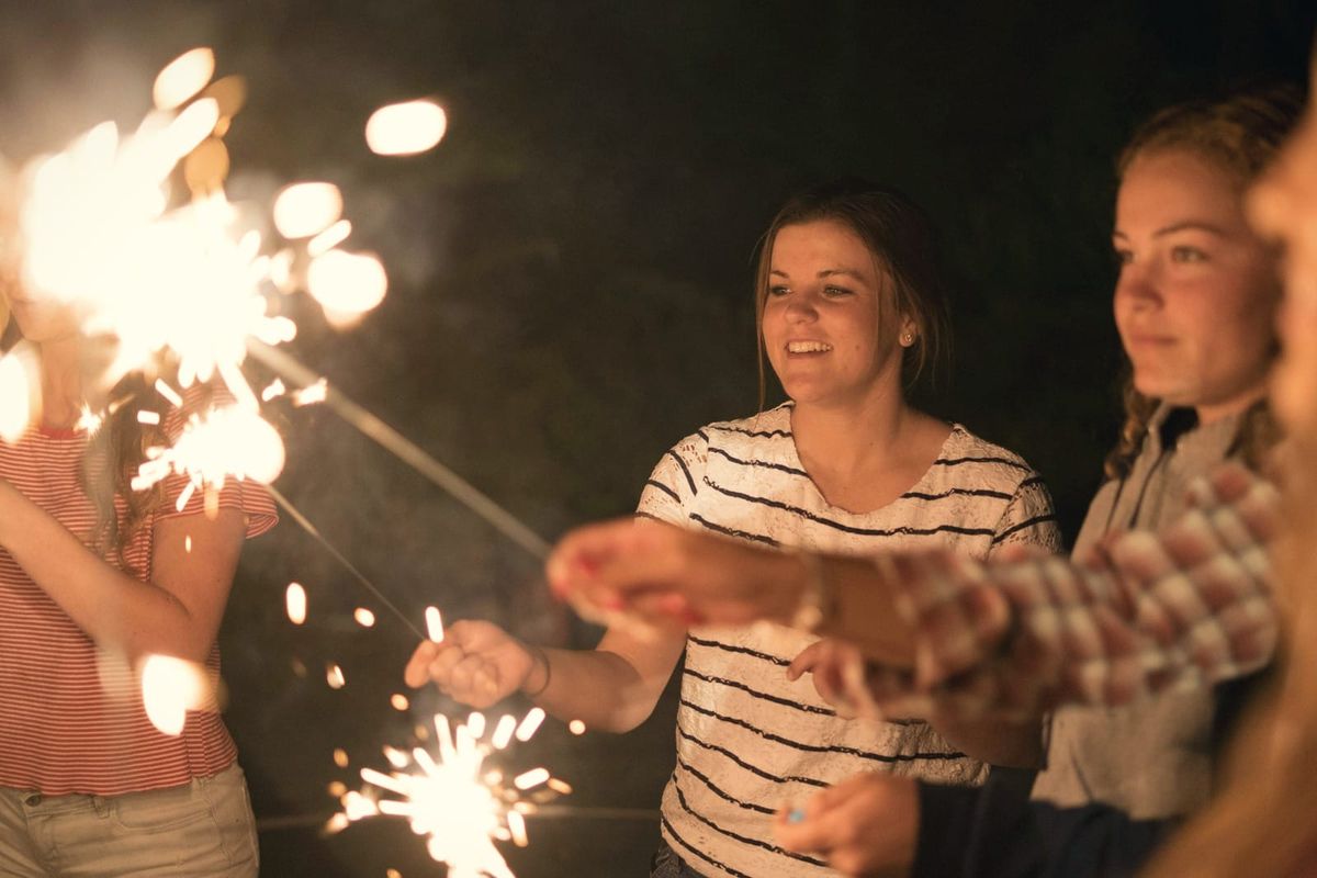 Friends smiling as they hold lit sparklers on a late-summer evening