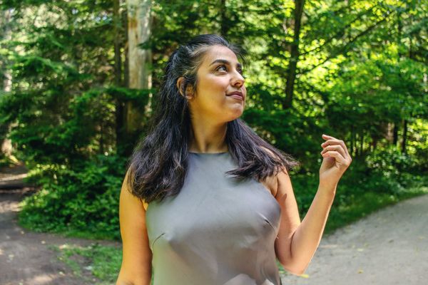 A woman looks up, smiling softly, on a sunlit green forest path in summer.