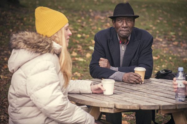 A young woman and an older man talking over coffee at an outdoor picnic table in autumn